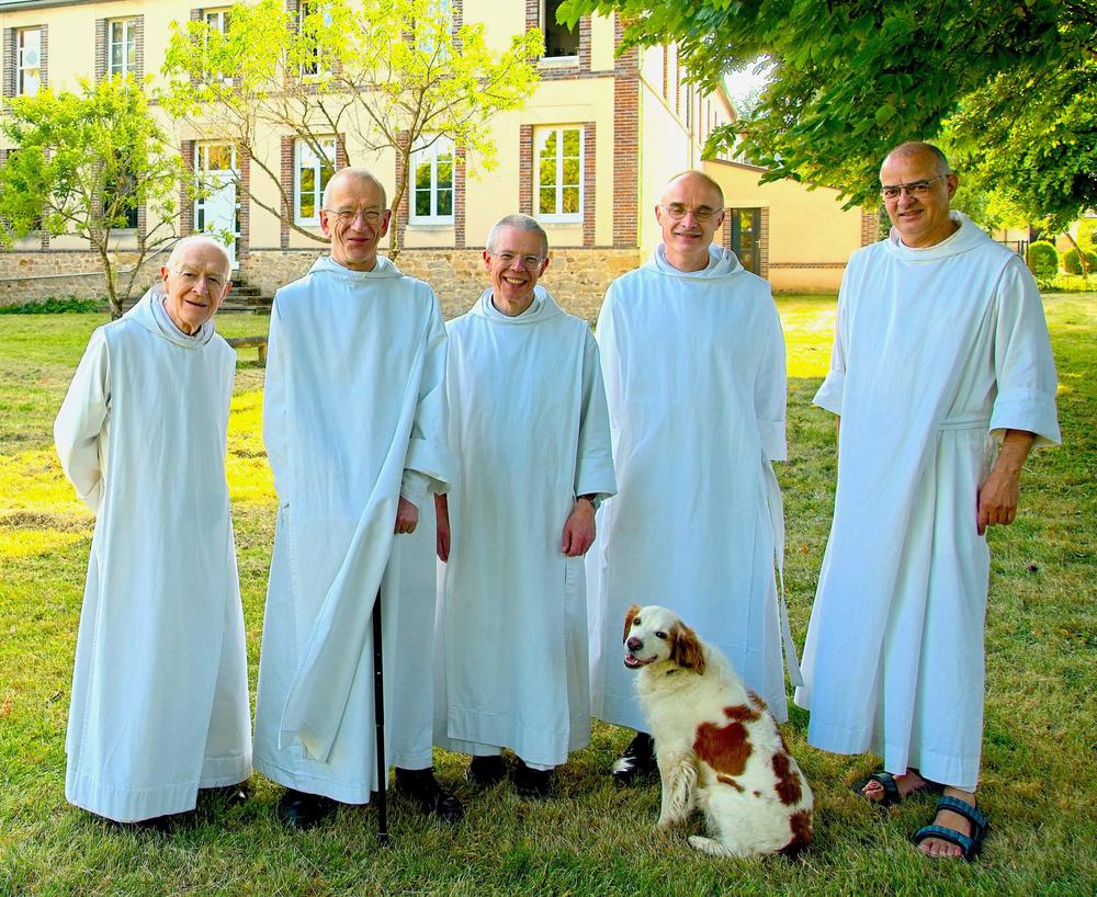 Cinq moines en robes blanches sont debout dans un jardin, avec un chien.