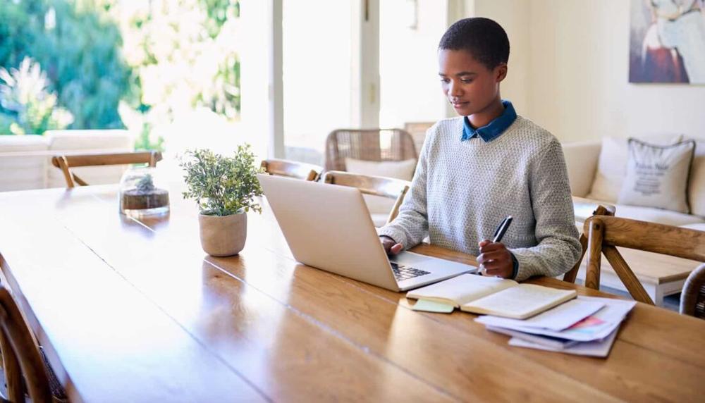 Une femme est assise à une table et travaille sur son ordinateur portable.