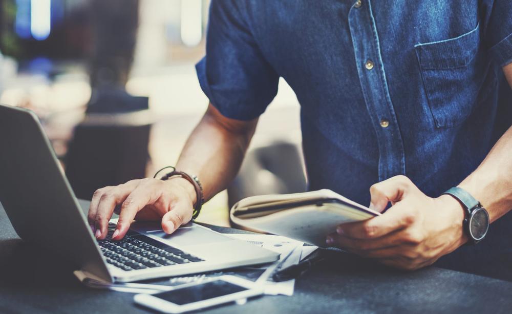 Un homme est assis à une table et travaille sur son ordinateur portable.