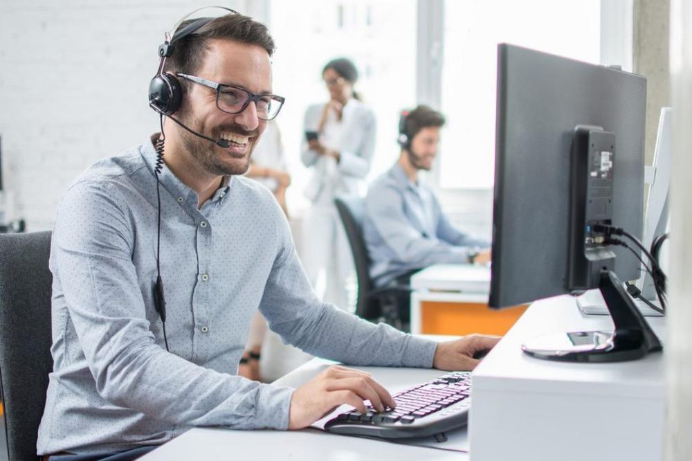 Un homme souriant avec un casque sur la tête est assis devant un ordinateur.