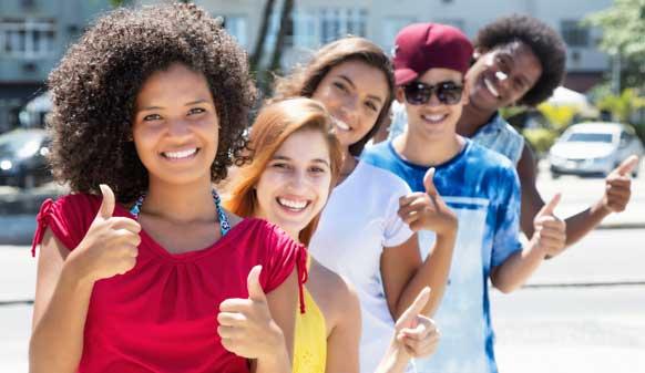 Une rangée de cinq jeunes multiethniques souriants avec leurs pouces levés.