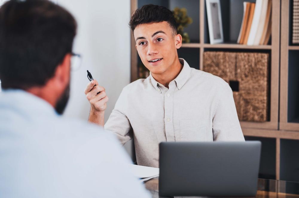 Un jeune homme est assis à une table et parle à un homme plus âgé.