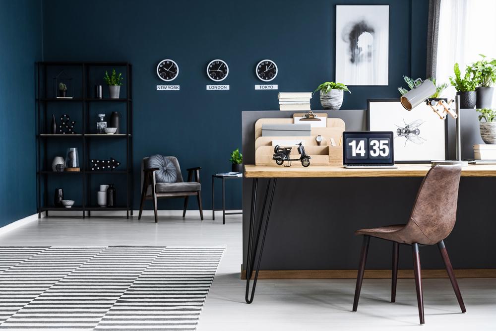 Une chaise en cuir marron, un bureau en bois, une horloge et des plantes vertes dans un bureau bleu.