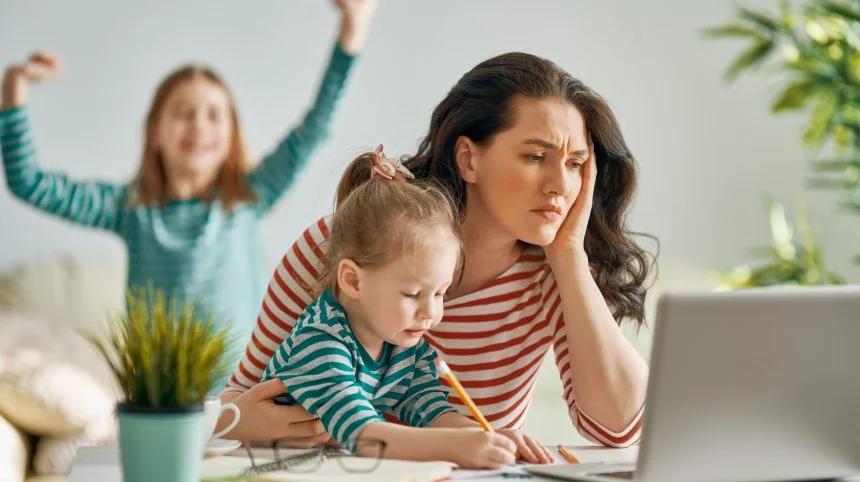 Une mère travaille sur son ordinateur portable avec sa fille à côté delle.